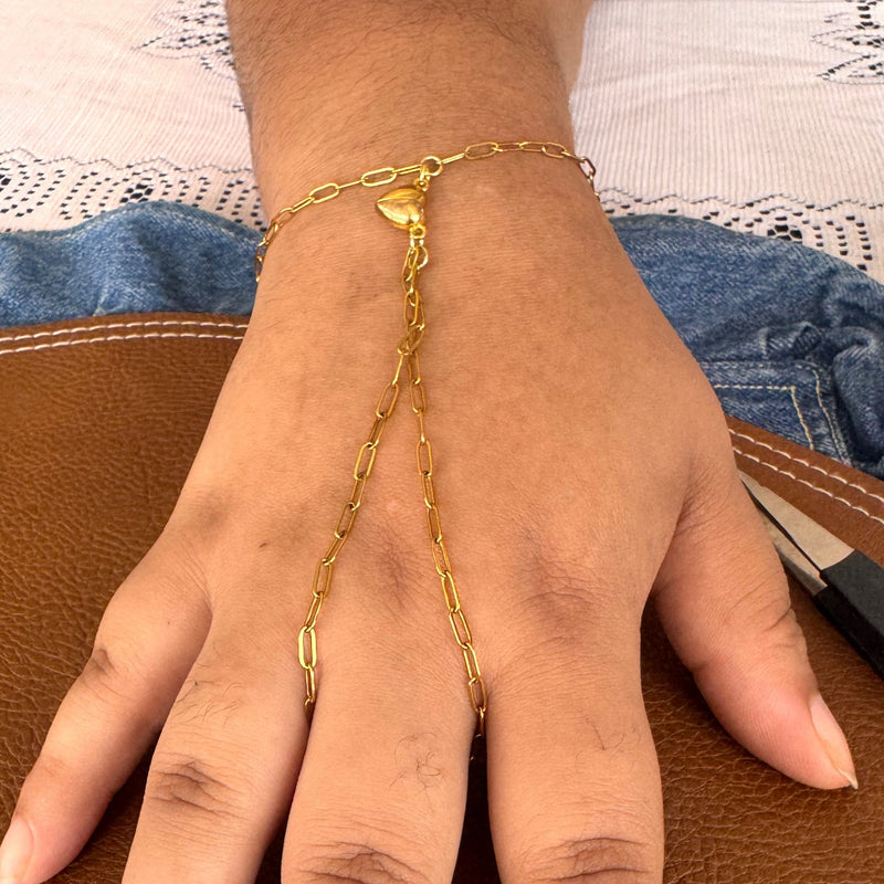 A gold chain hand bracelet worn on a person's hand, resting on a brown leather surface.